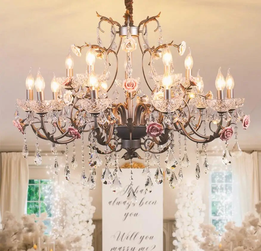 Detail shot of the chandelier's arm, highlighting the texture of the gold finish, the delicate pink ceramic rose, and a sparkling teardrop crystal.