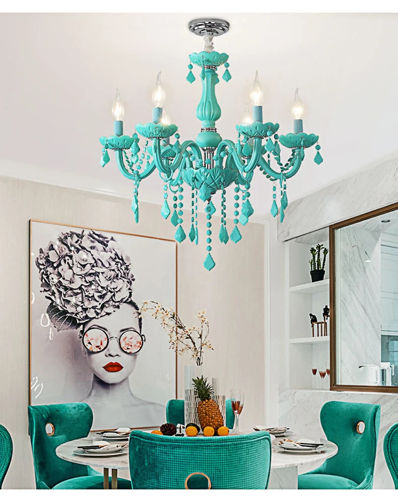 A cyan crystal chandelier hanging above a dining table set with teal velvet chairs, in a room with modern artwork.