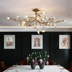 Gold chandelier hanging above a dining table with dark walls and framed pictures.
