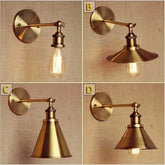 Close-up of a gold cone shade wall sconce with an exposed Edison bulb and adjustable arm against a textured wall.