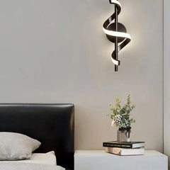 Modern wall light fixture above a bed with books and flowers on a nightstand.