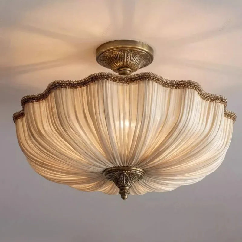 Close-up of a beige fabric pleated semi-flush ceiling light with ornate gold-toned hardware