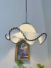 White lampshade with black trim hanging above a painting on a light blue wall.