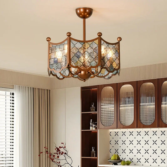Bronze geometric paneled chandelier with multi-colored glass shades hanging in a dining area above a wooden cabinet.