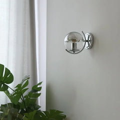 Modern wall sconce with glass shade on a white wall next to a plant