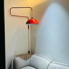 Red folding retractable wall lamp with a dome shade mounted on a light-colored wall above a white sofa, casting a warm light.