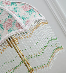 Decorative lampshade with floral pattern and gold fringe on a plain background