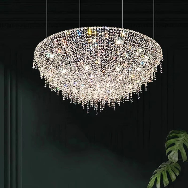 Crystal chandelier hanging against a dark background with a plant on the side.