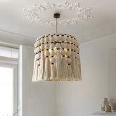 Close-up of a handwoven wicker drum pendant light with cream-colored tassels hanging from a white ceiling with decorative molding.