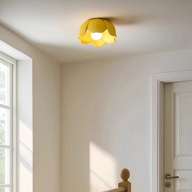 A yellow ceramic flower-shaped semi-flush ceiling light mounted on a white ceiling in a room with a window and doorway.