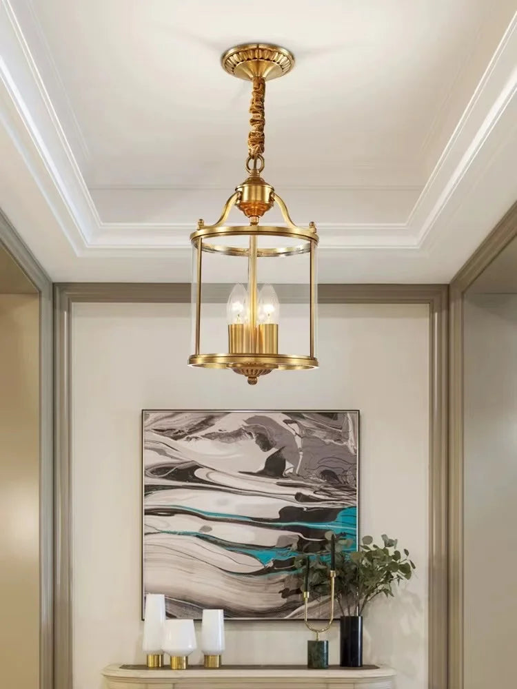 Gold lantern pendant light with clear glass shade hanging from a ceiling with a decorative chain.