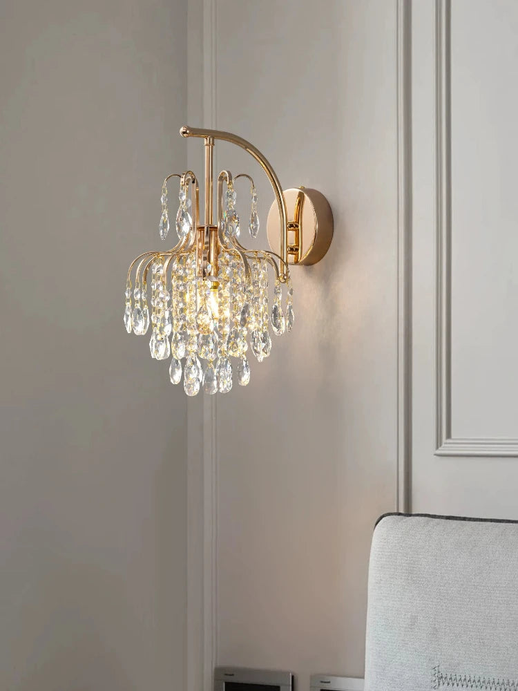Close-up of a gold wall sconce with clear teardrop crystals reflecting light.