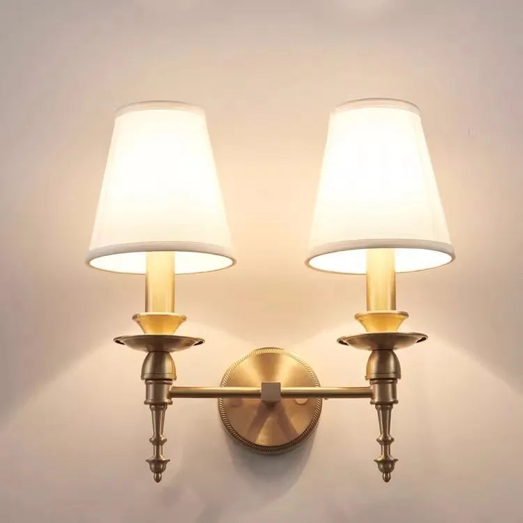 Wall-mounted lamp with two white shades and brass fixtures on a light gray wall.