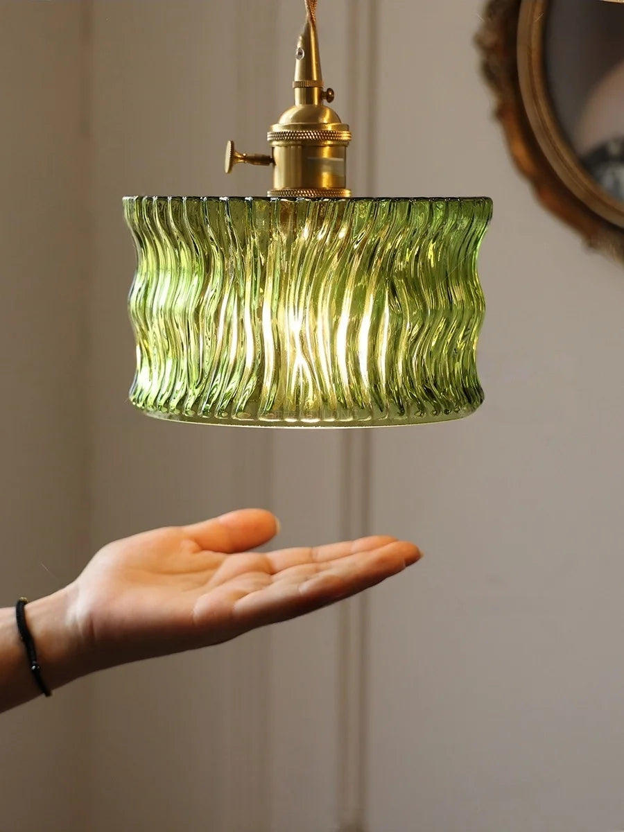 Green ribbed pendant light with brass fixture held by a hand against a neutral background
