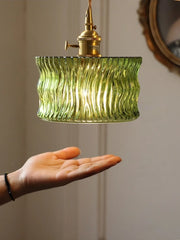 Green ribbed pendant light with brass fixture held by a hand against a neutral background