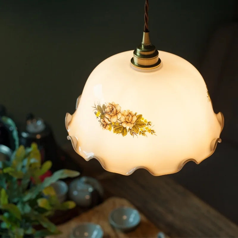 Decorative pendant light with floral design on a dark background. Adjustable LED brass kitchen pendant with scallop edge.