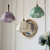 Three decorative pendant lights with colourful glass shades hanging against a white wall. Modern glass mosaic hanging lamp for kitchen, dining, or living