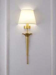 Gold wall sconce with a white lampshade on a gray wall.