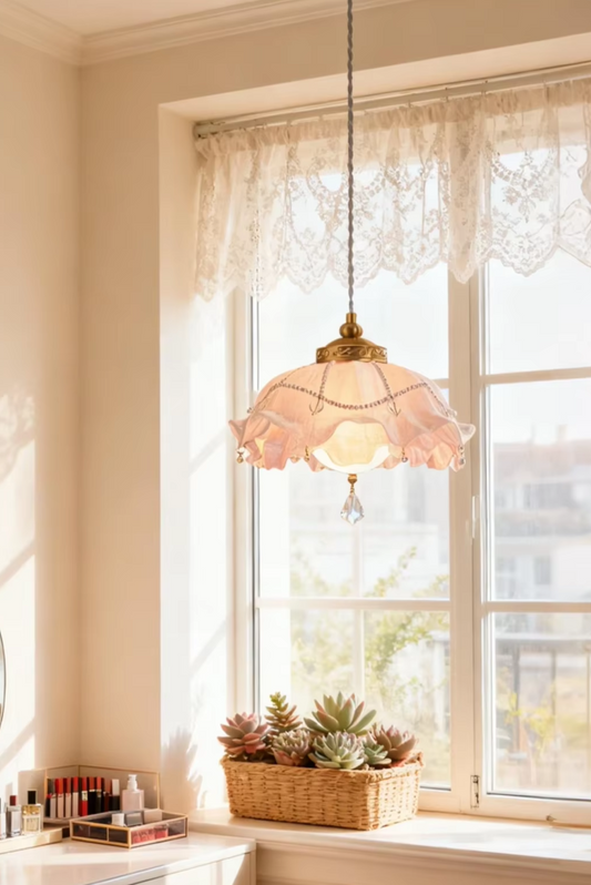 Pink floral lampshade with crystal accents hanging in front of a window with lace curtains.
