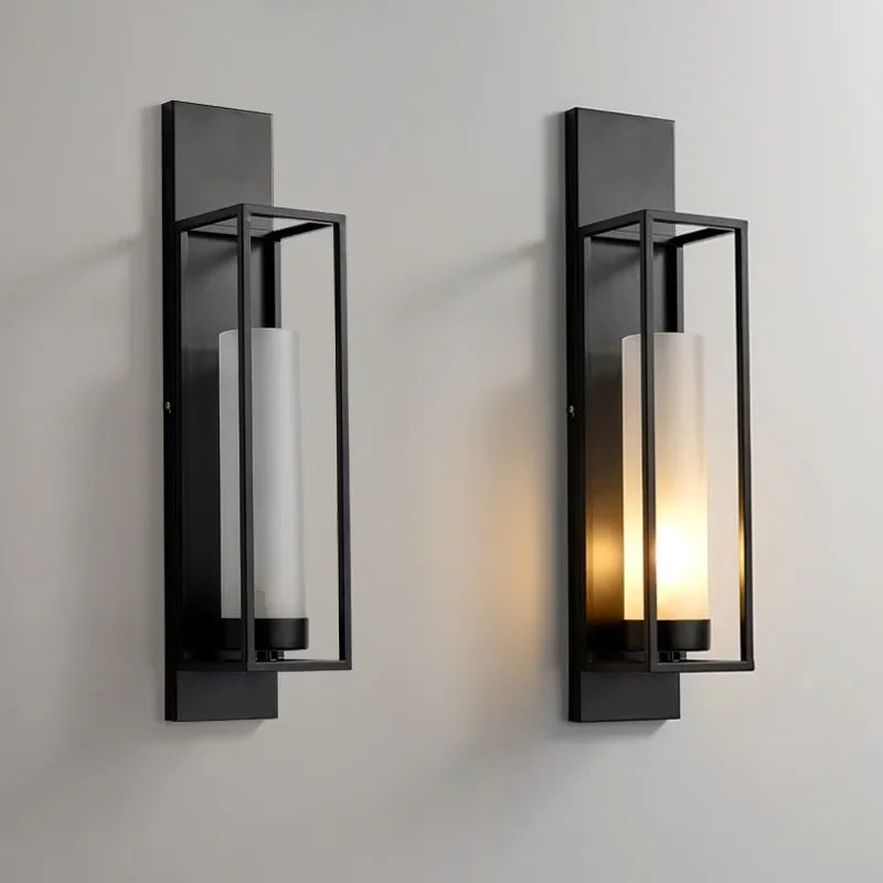 Two black wall sconces with glass covers on a light gray wall.