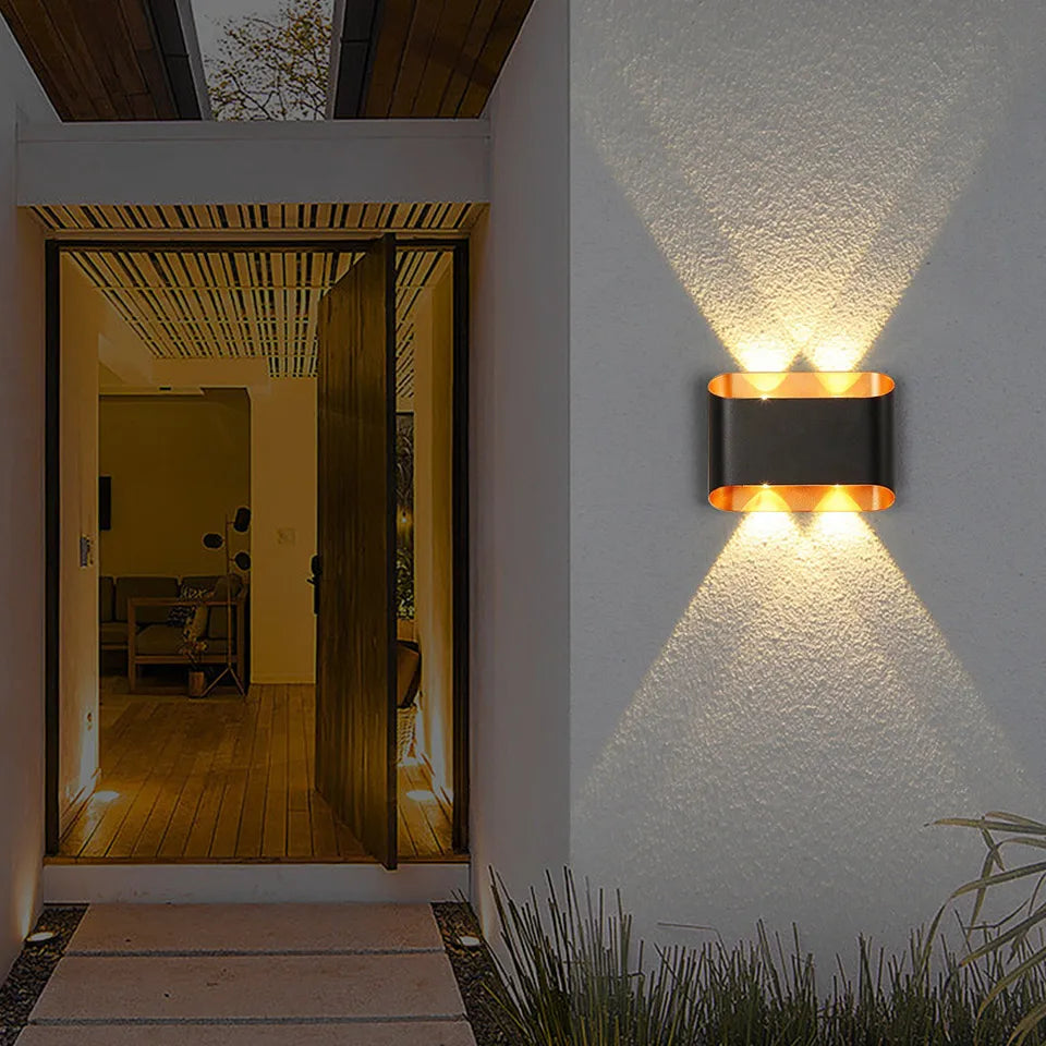 “Pair of outdoor LED wall sconces illuminating a white exterior garden wall.”