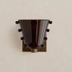 Decorative wall sconce with a dark brown glass shade and black accents on a beige wall.