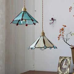 Two stained glass pendant lights hang from the ceiling, with a decorative frame and a plant in the background. Colourful copper and glass pendant light with a floral design.