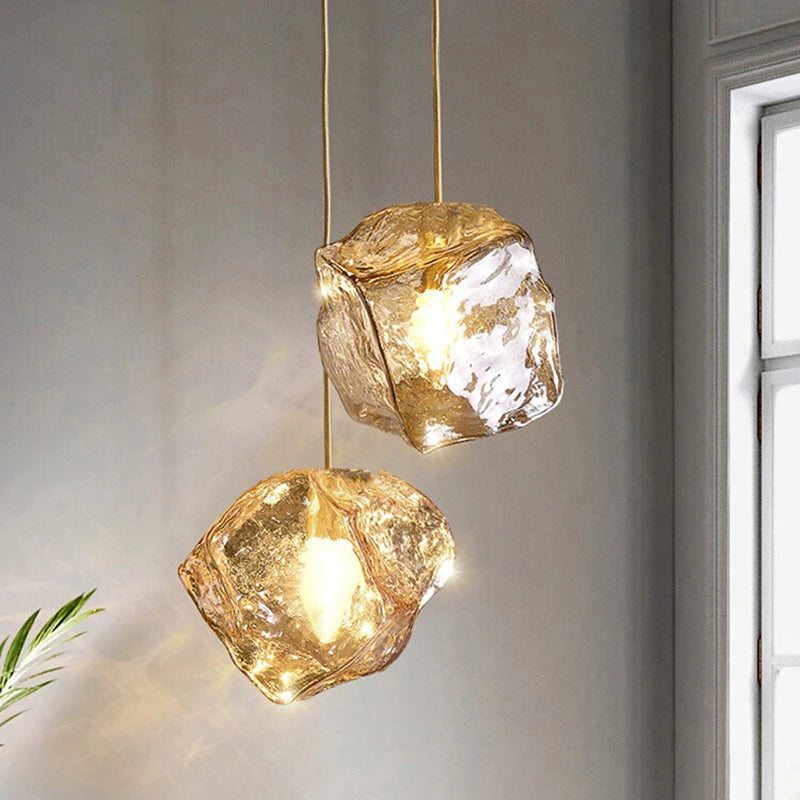 Two gold pendant lights with organic lava glass stones hanging against a neutral wall