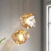 Two gold pendant lights with organic lava glass stones hanging against a neutral wall