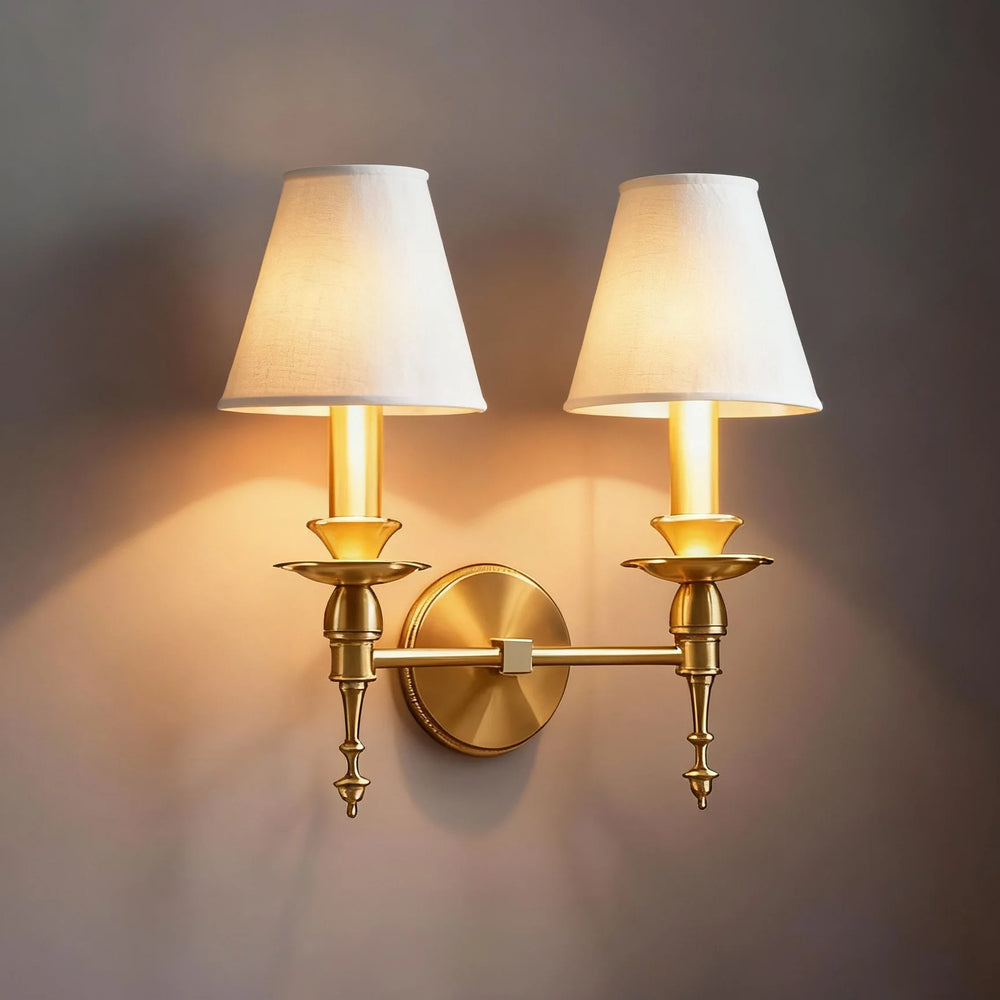 Double wall sconce with gold brackets and white lampshades on a dark wall.