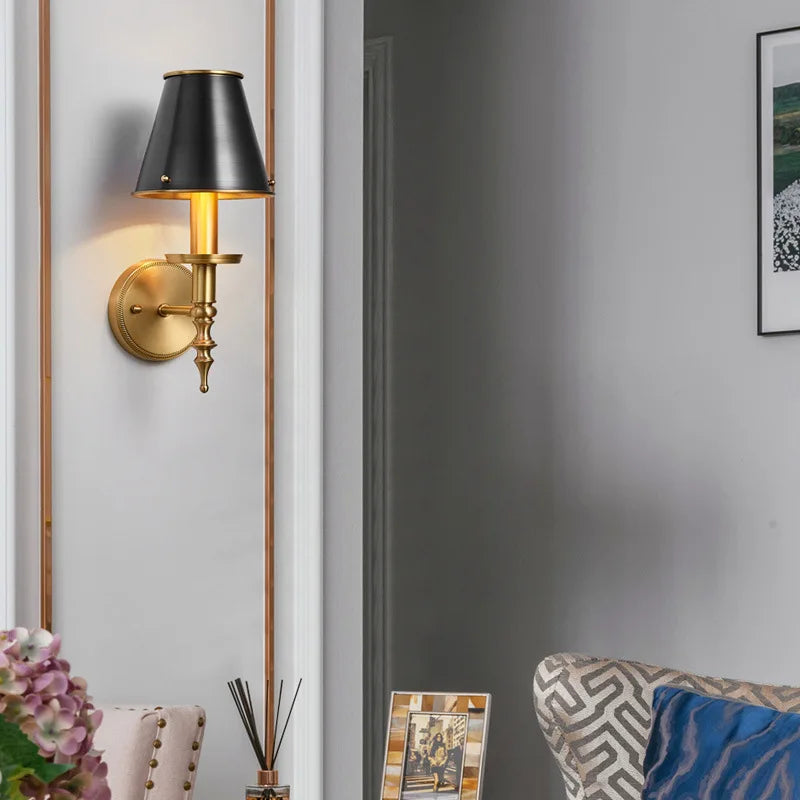 Wall-mounted lamp with black shade and gold base in a room setting.