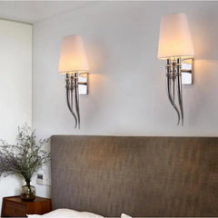 Two wall sconces with lampshades on a wall above a bed.