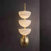 Wall-mounted light fixture with three tiered glass shades on a dark background