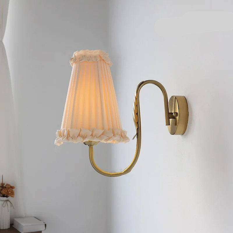 French retro wall lamp with pleated fabric shade and brass arm mounted on white wall.
