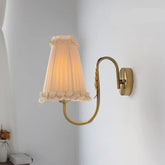 French retro wall lamp with pleated fabric shade and brass arm mounted on white wall.