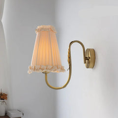 French retro wall lamp with pleated fabric shade and brass arm mounted on white wall.