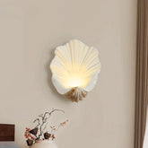 Shell-shaped wall lamp on a beige wall with a decorative item below.