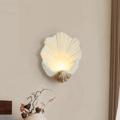 Shell-shaped wall lamp on a beige wall with a decorative item below.