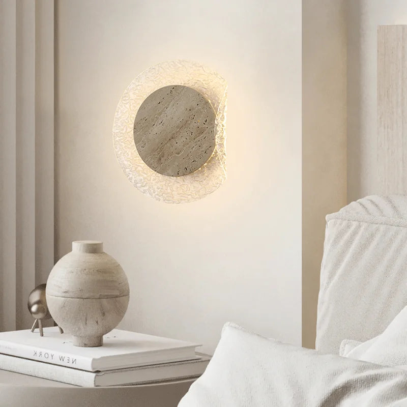 Round wall light fixture in a modern interior setting with books and a vase on a table.