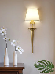 Gold wall sconce with white flowers in vases on a wooden surface against a beige wall.