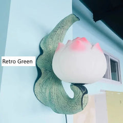 Decorative wall light with retro green base and pink lampshade on a light blue background.