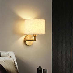 Wall-mounted lamp with gold fixture and white shade on a neutral wall.