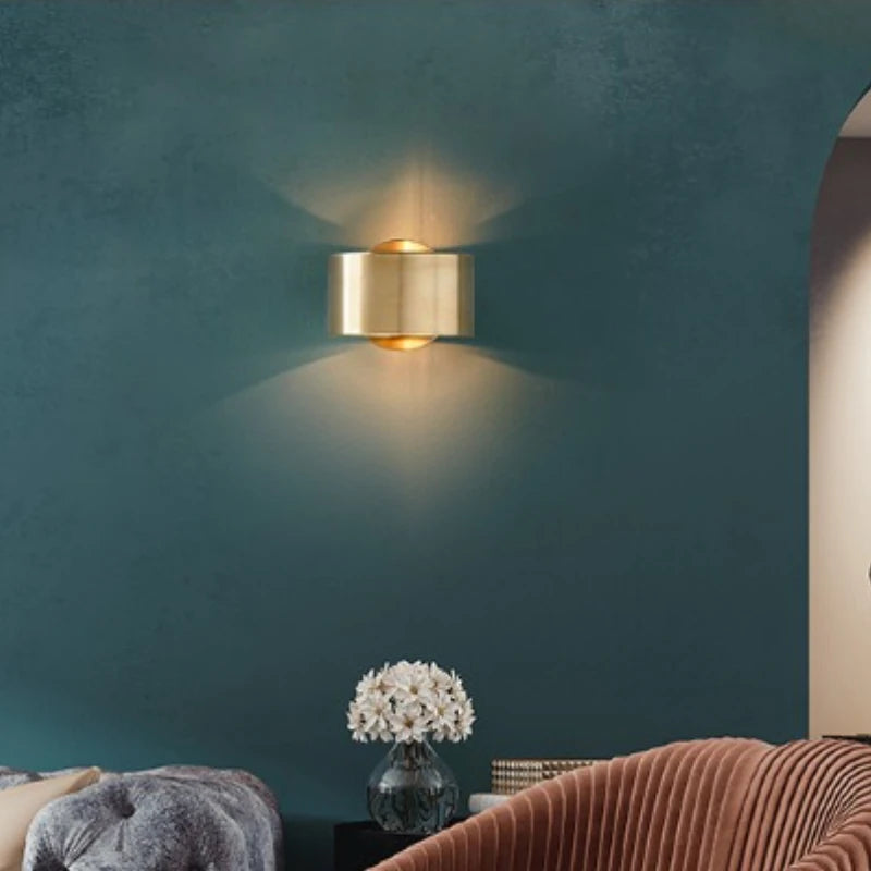 Gold wall sconce on a teal wall with a vase and cushions on a table below.