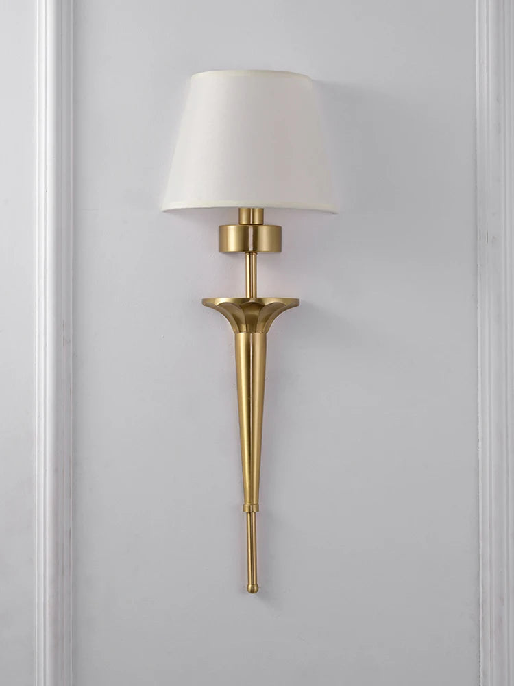 Gold wall sconce with a white lampshade on a gray wall.