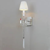 Wall-mounted lamp with crystal details and a white shade on a gray wall.