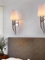 Two wall sconces with lampshades on a light gray wall above a bed.