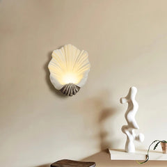 Shell-shaped wall light fixture on a beige wall with a sculpture and plant in the foreground.