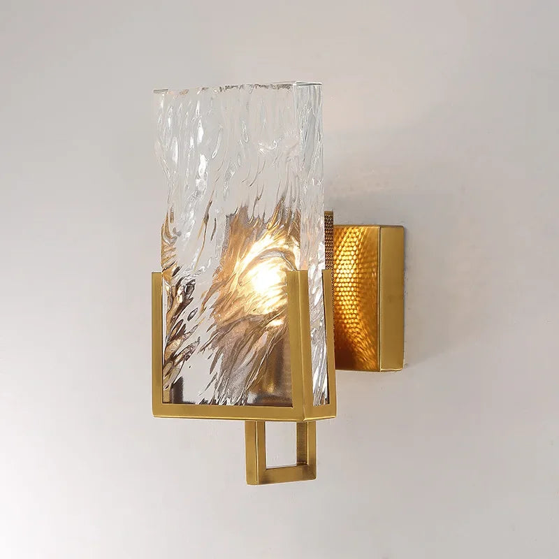 Wall-mounted light fixture with gold frame and textured glass shade on a plain background