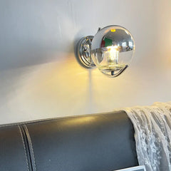 Wall-mounted lamp with glass shade on a white wall above a gray sofa.