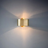 Gold wall-mounted light fixture casting a warm glow on a gray wall.